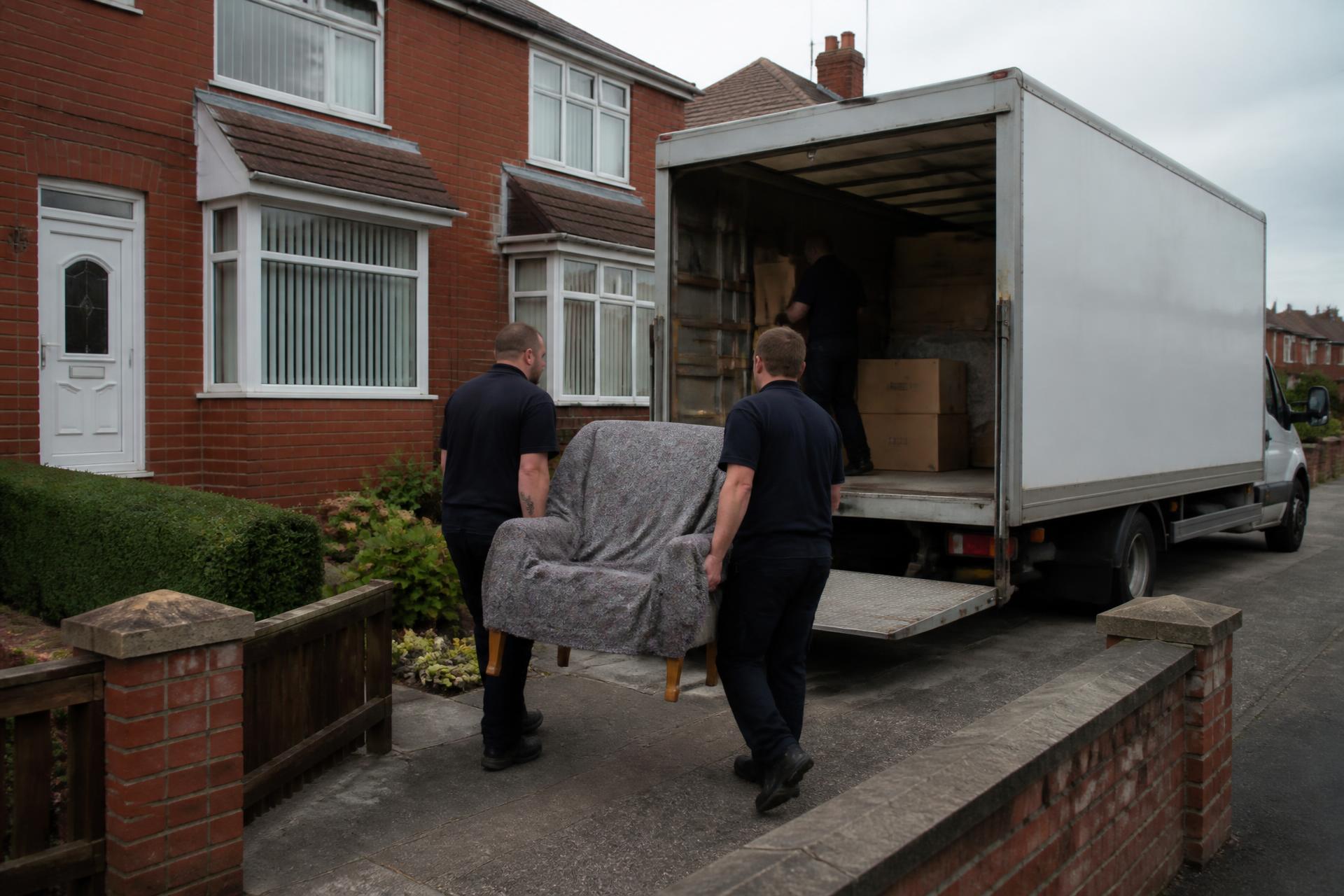 Mersey Removals team loading a blanket-wrapped armchair into a removals van outside a house